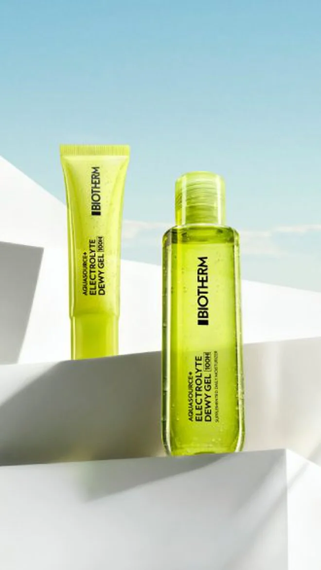 alt="Neon yellow-green transparent gel bottle and matching travel-size tube displayed on white geometric surfaces against a blue sky."